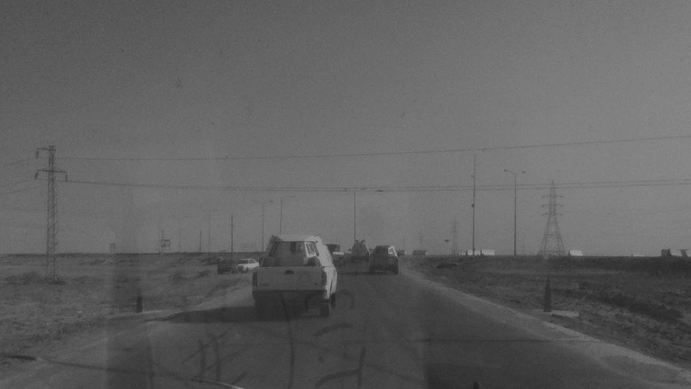 A convoy of vehicles on an open highway, seen through the windscreen of a following vehicle