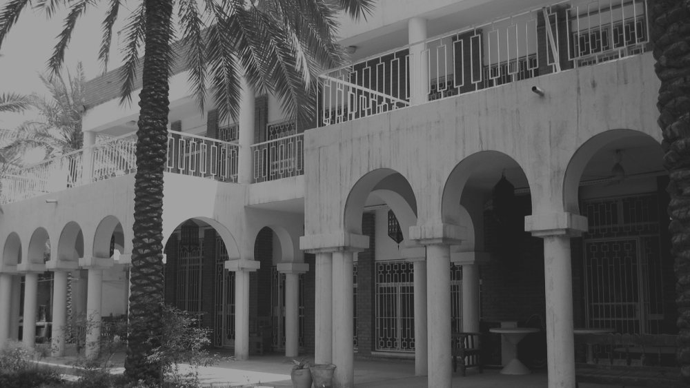 A walled residential compound with an arcaded ground floor and first-floor balconies, seen from its garden